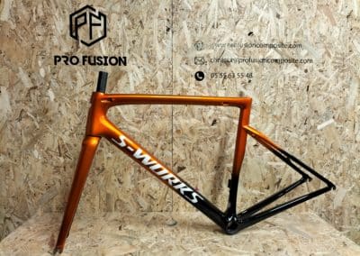 cadre de vélo peint avec une Peinture orange custom personnalisée tarmac SL6 SPECIALIZED, posé sur une structure en OSB et devant un panneau en OSB, avec le logo de profusion composite en haut à gauche.